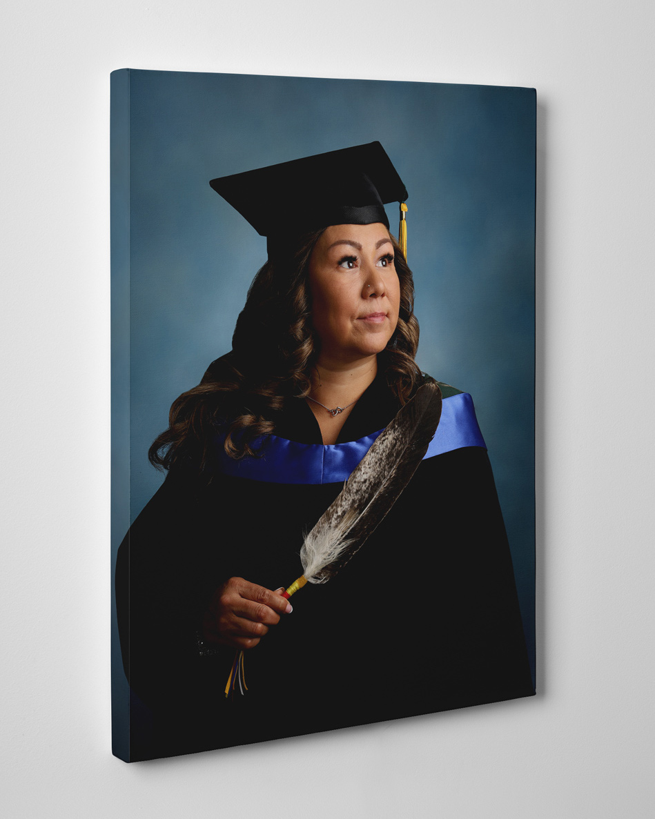 Canvas printed mounted on wall showing a woman in graduation attire looking away holding an Eagle feather