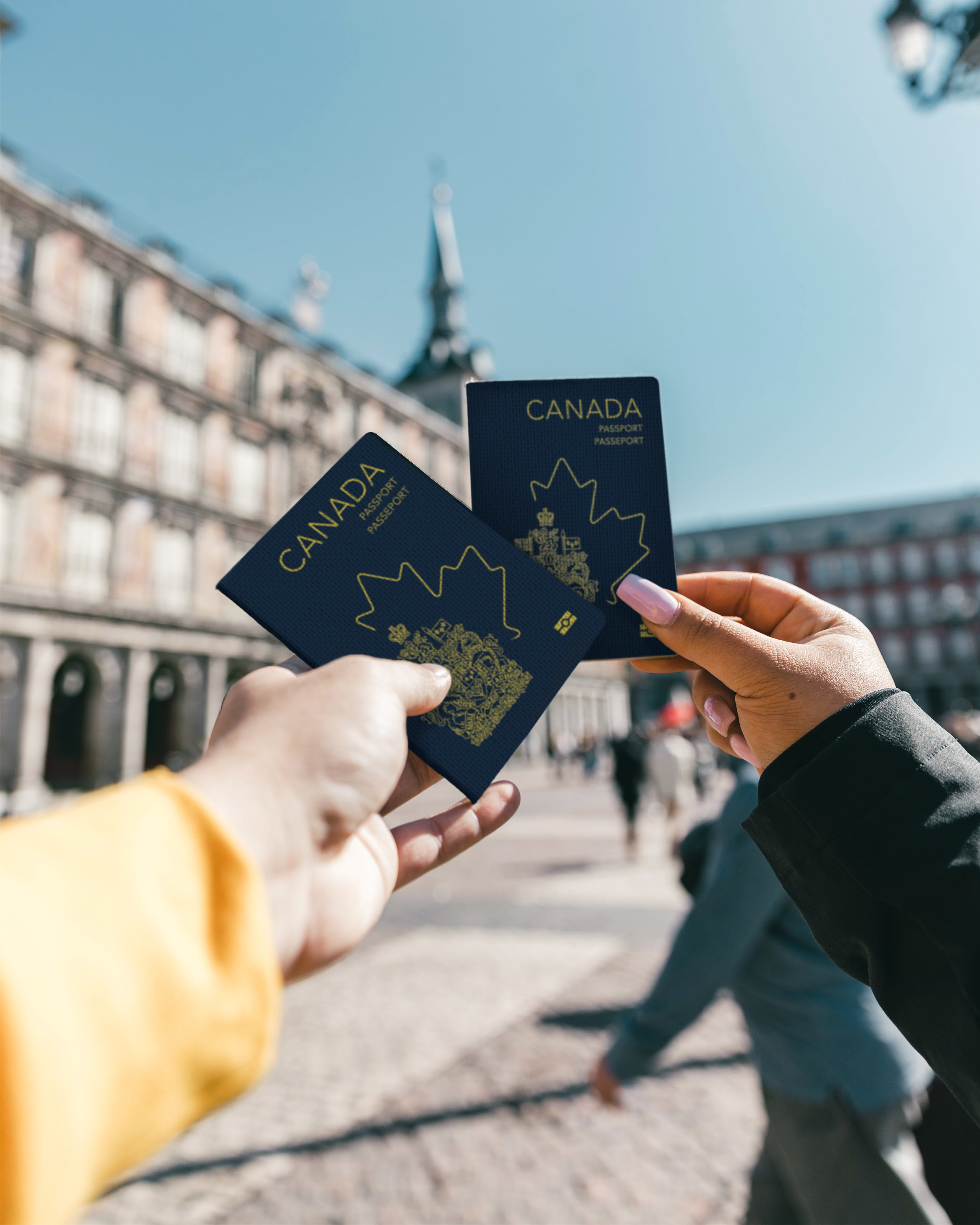 Two peoples hands holding up their passports infront of an out of focus building